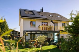 Vista sulla metà di una casa bifamiliare nel verde, sul cui tetto sono installati alcuni moduli solari 