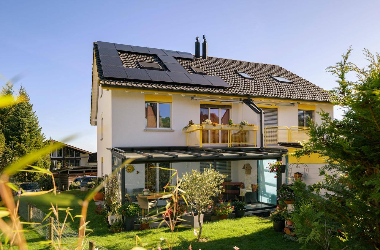 Blick auf eine Doppelhaushälfte im Grünen, die Solarmodule auf ihrem Dach trägt 