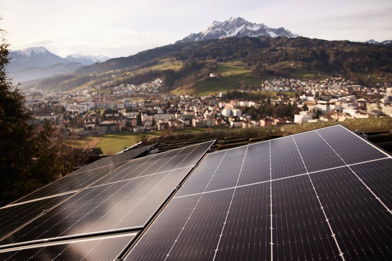 Dach mit montierten Solarmodulen vor einem Bergpanorama. 