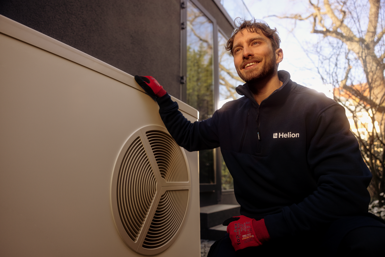 Un tecnico di Helion mentre installa una pompa di calore sulla parete esterna di una casa. 