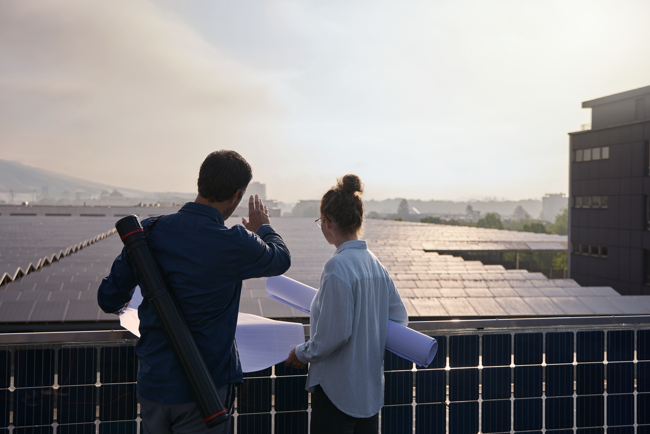 Une femme et un homme se tiennent devant une grande installation photovoltaïque et discutent des plans de construction. 