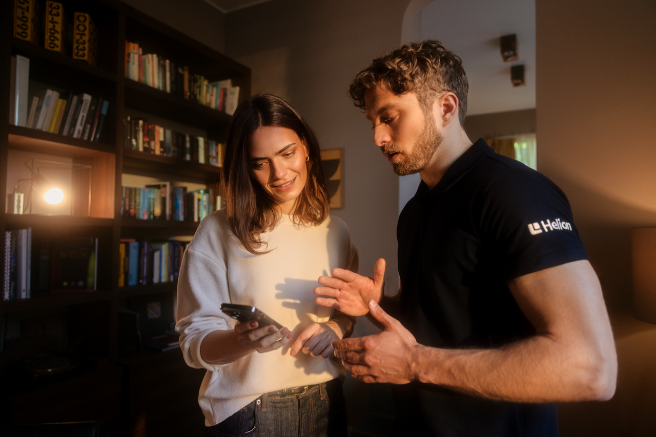 Eine Frau und ein Mann schauen auf ein Handy, sie stehen in einem Wohnzimmer. 